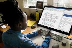 Young person using a wireless keyboard to work on a document in Microsoft Word on a large desktop monitor